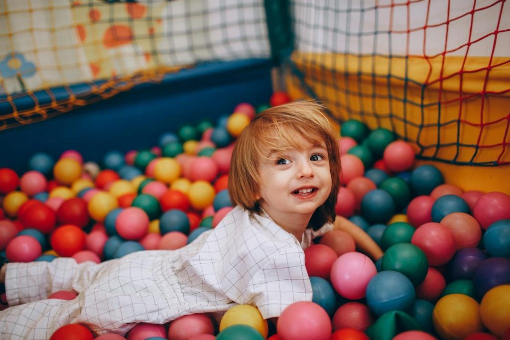 Adorable young child smiling in a vibrant ball pit at an indoor playground setting.