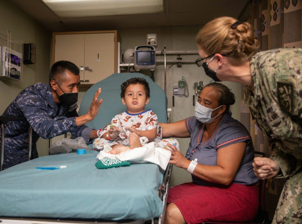 A child sits on a medical bed with adults around.