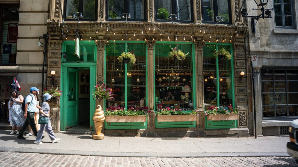 Green storefront with people walking by on cobblestone street