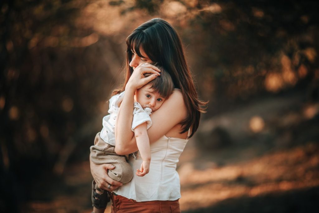 A mother lovingly holds her child outdoors in warm light, creating a heartwarming scene.