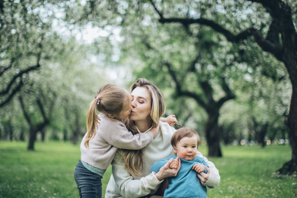 A warm family moment as a mother holds her children in a blooming spring park.