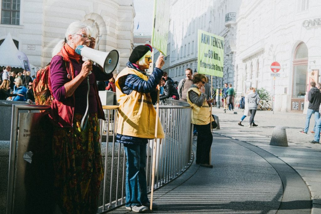A vibrant protest scene in Vienna with diverse participants holding signs and a megaphone.