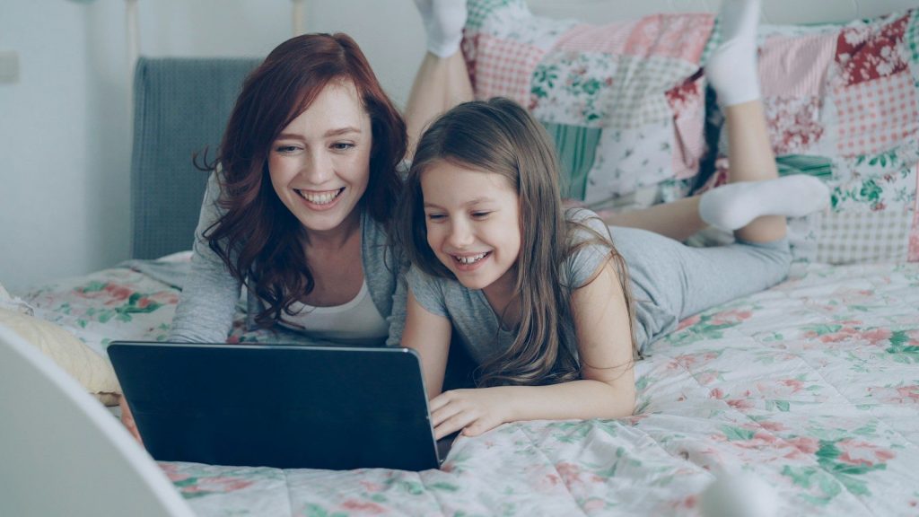 Mother and daughter laugh while using a laptop