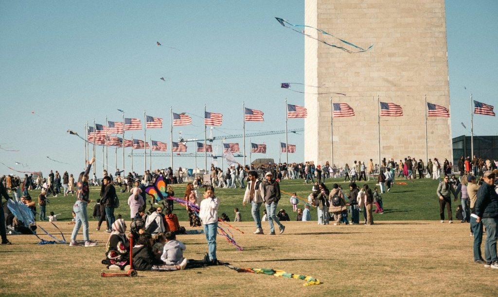 People flying kites near washington monument with flags