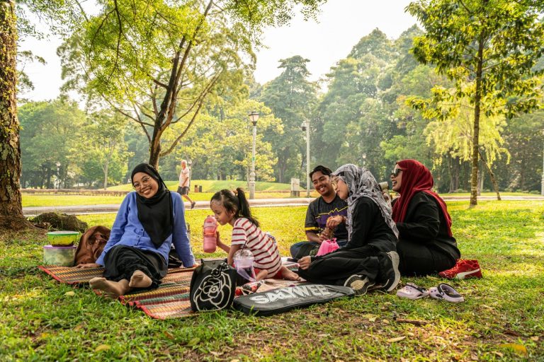 A family on a picnic mat in a sunlit park with trees