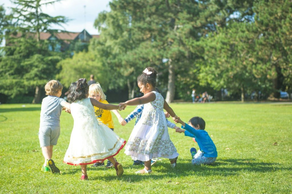 A group of children holding hands in a circle on a sunny park lawn