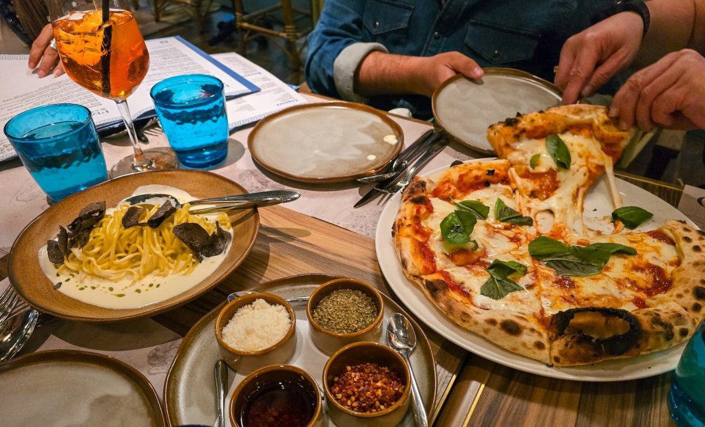 People eating pizza and pasta with truffle at a restaurant table