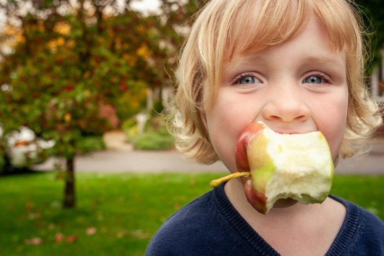 Young child with a bitten apple in mouth